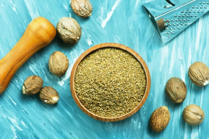 nutmeg powder in wooden bowl with nutmeg seeds around it.